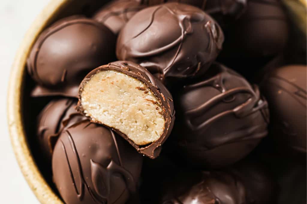 A bowl of chocolate truffles, with one truffle cut in half to show a creamy, light-colored filling inside.