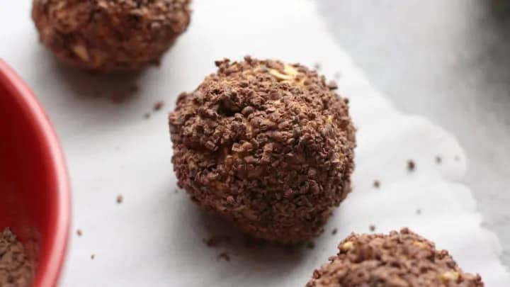 A close-up of a chocolate-coated dessert ball with a rough texture, resting on a sheet of parchment paper.