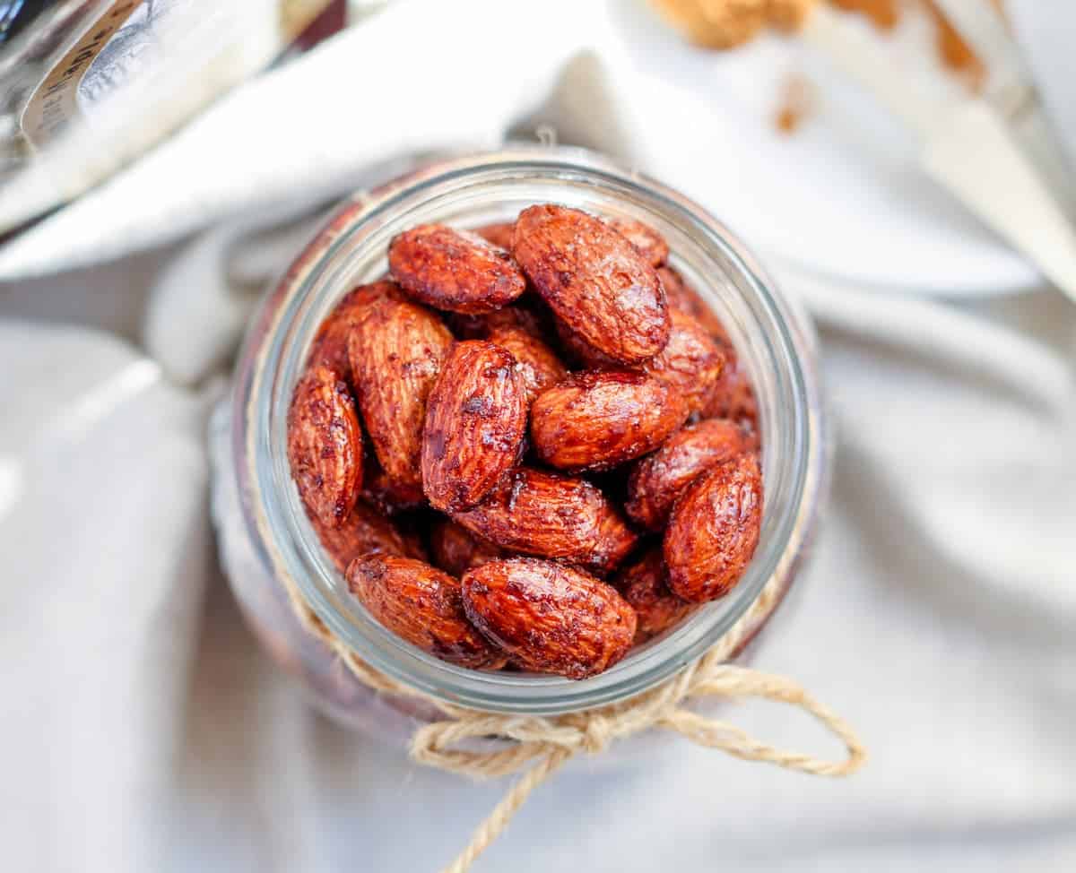 A glass jar filled with roasted almonds, tied with a piece of twine, sits on a light-colored cloth.