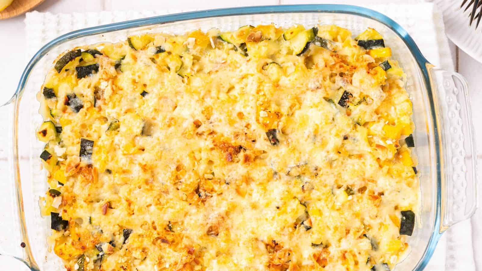 A glass baking dish filled with a baked vegetable casserole topped with melted cheese, featuring visible pieces of zucchini and yellow bell pepper.