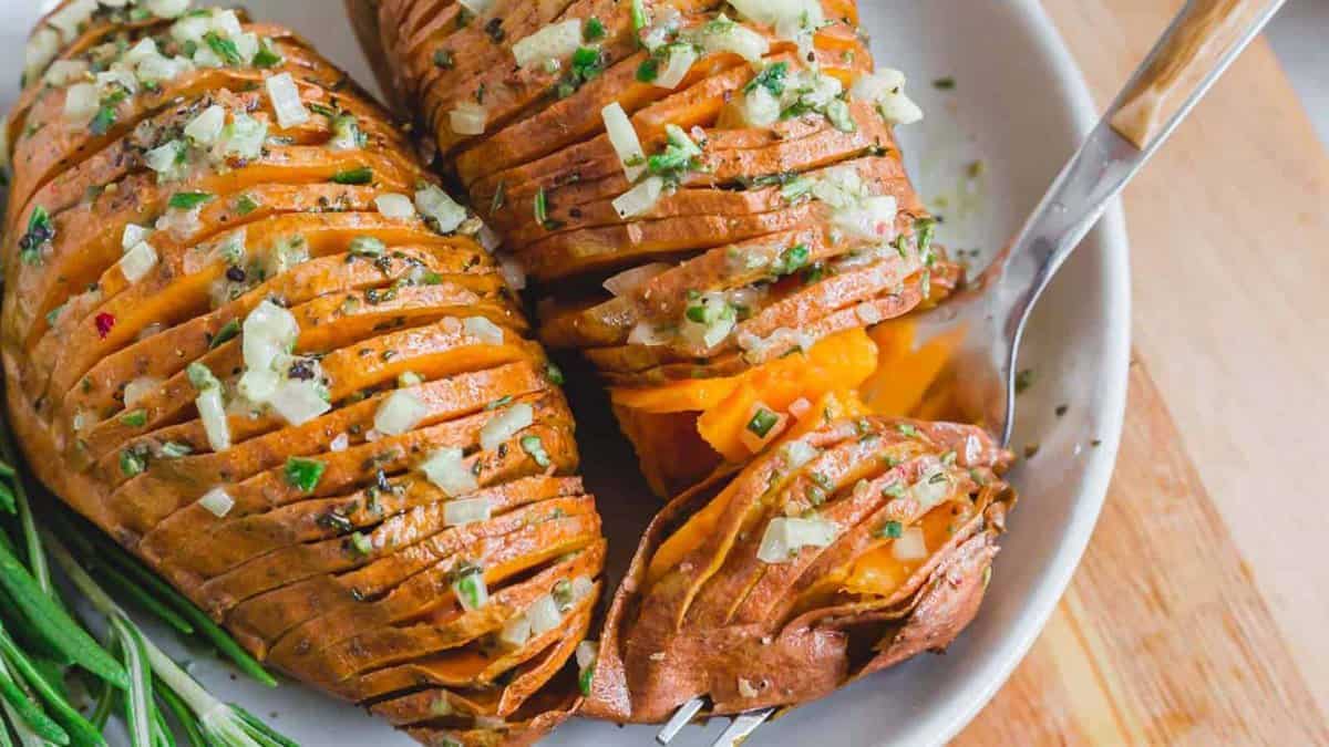 Sliced baked sweet potatoes topped with chopped herbs and diced onions, served on a white plate with a fork.