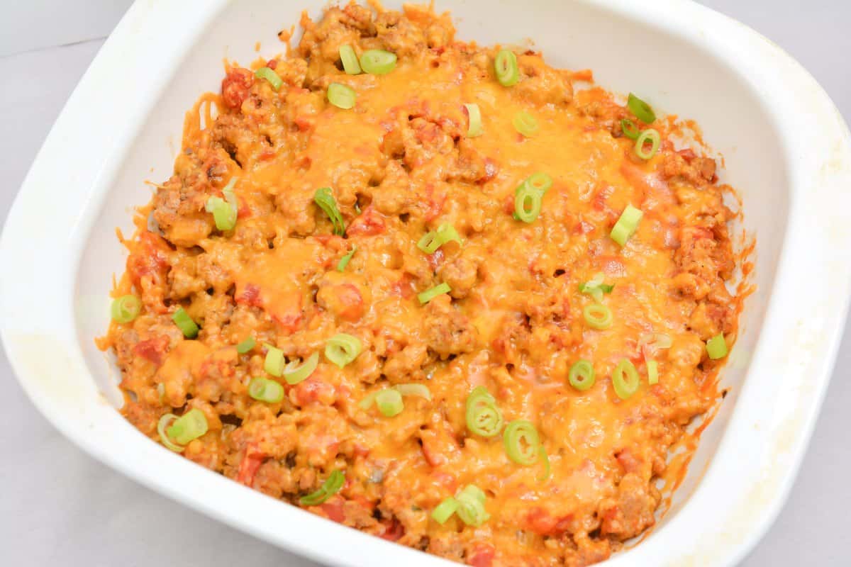 A white baking dish filled with a cheesy ground beef casserole topped with chopped green onions.