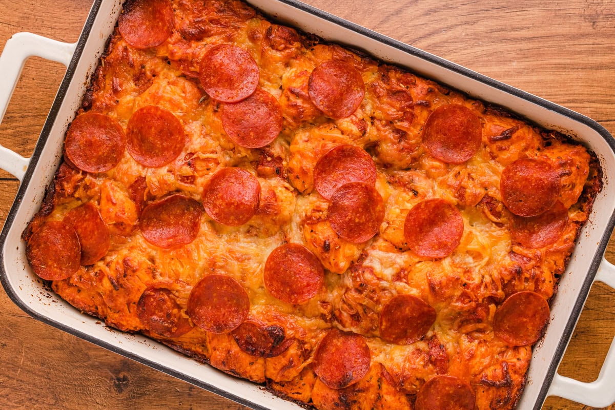 A baked casserole dish filled with cheesy bread topped with slices of pepperoni on a wooden surface.