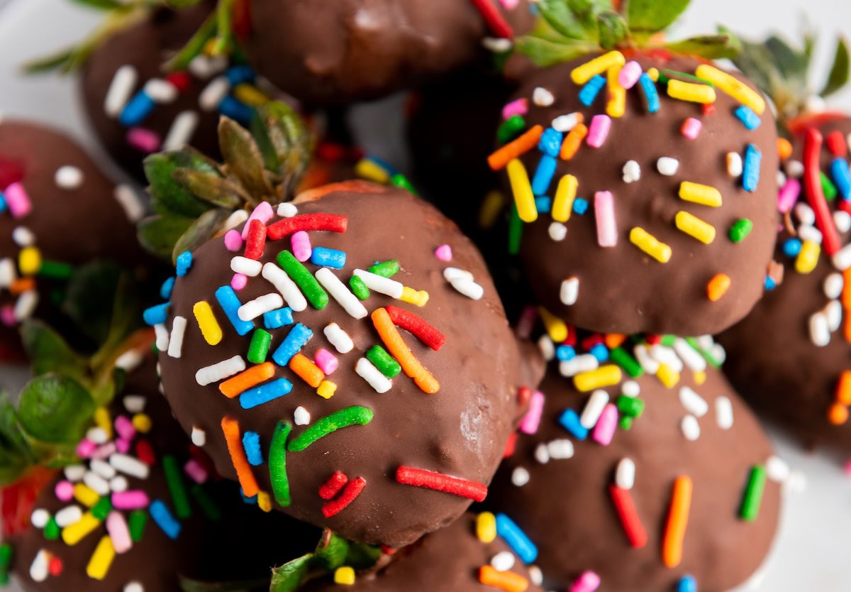 Chocolate-covered strawberries topped with colorful sprinkles are stacked together on a plate.