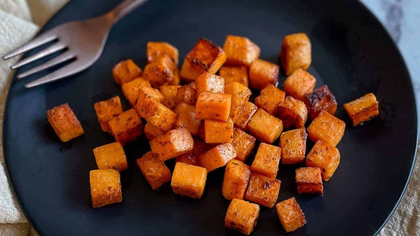A black plate with roasted butternut squash cubes, seasoned and slightly browned, next to a fork.