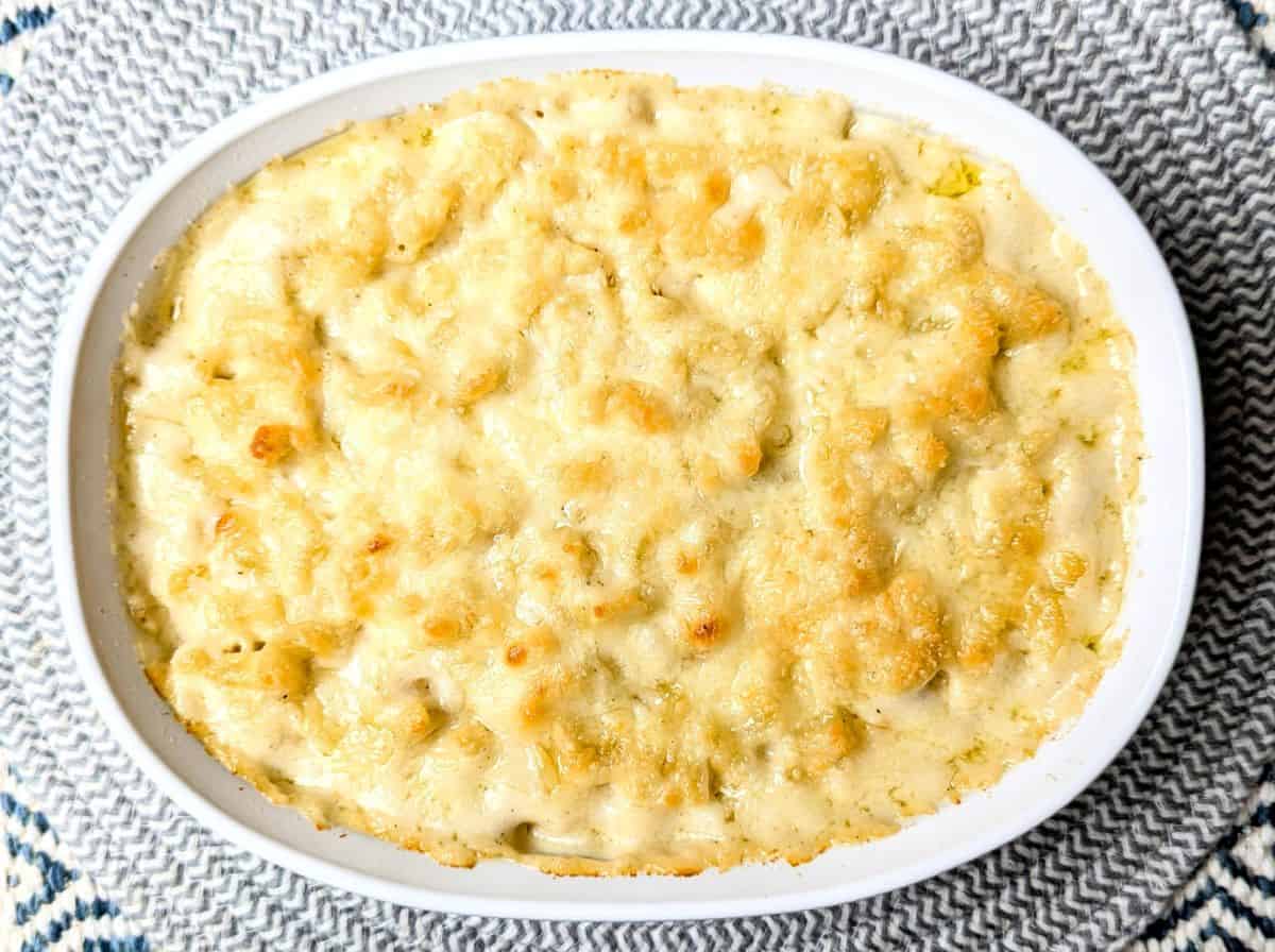 Baked macaroni and cheese in a white oval dish, topped with melted golden cheese, placed on a patterned placemat.