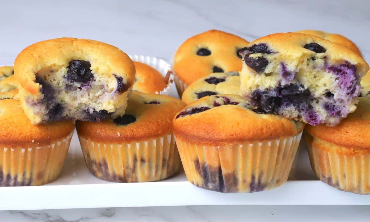 A tray of blueberry muffins, some whole and some with bites taken out, displayed on a white surface.
