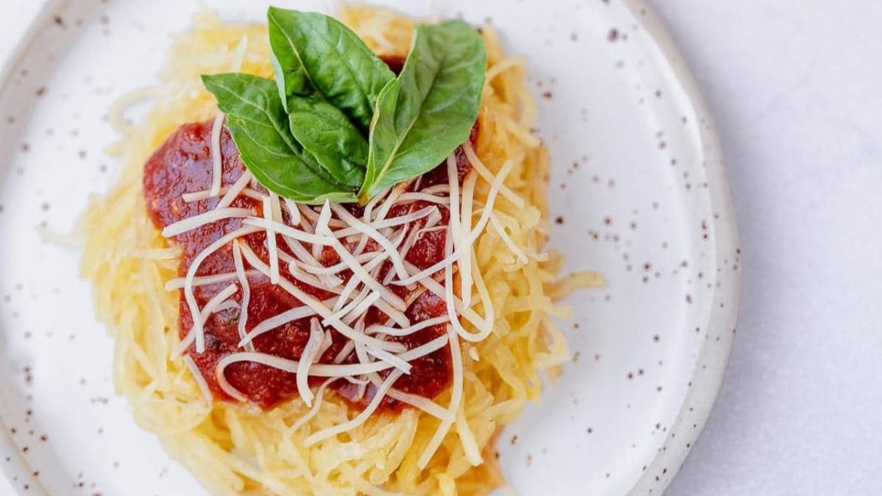 A plate of spaghetti squash topped with marinara sauce, shredded cheese, and fresh basil leaves.
