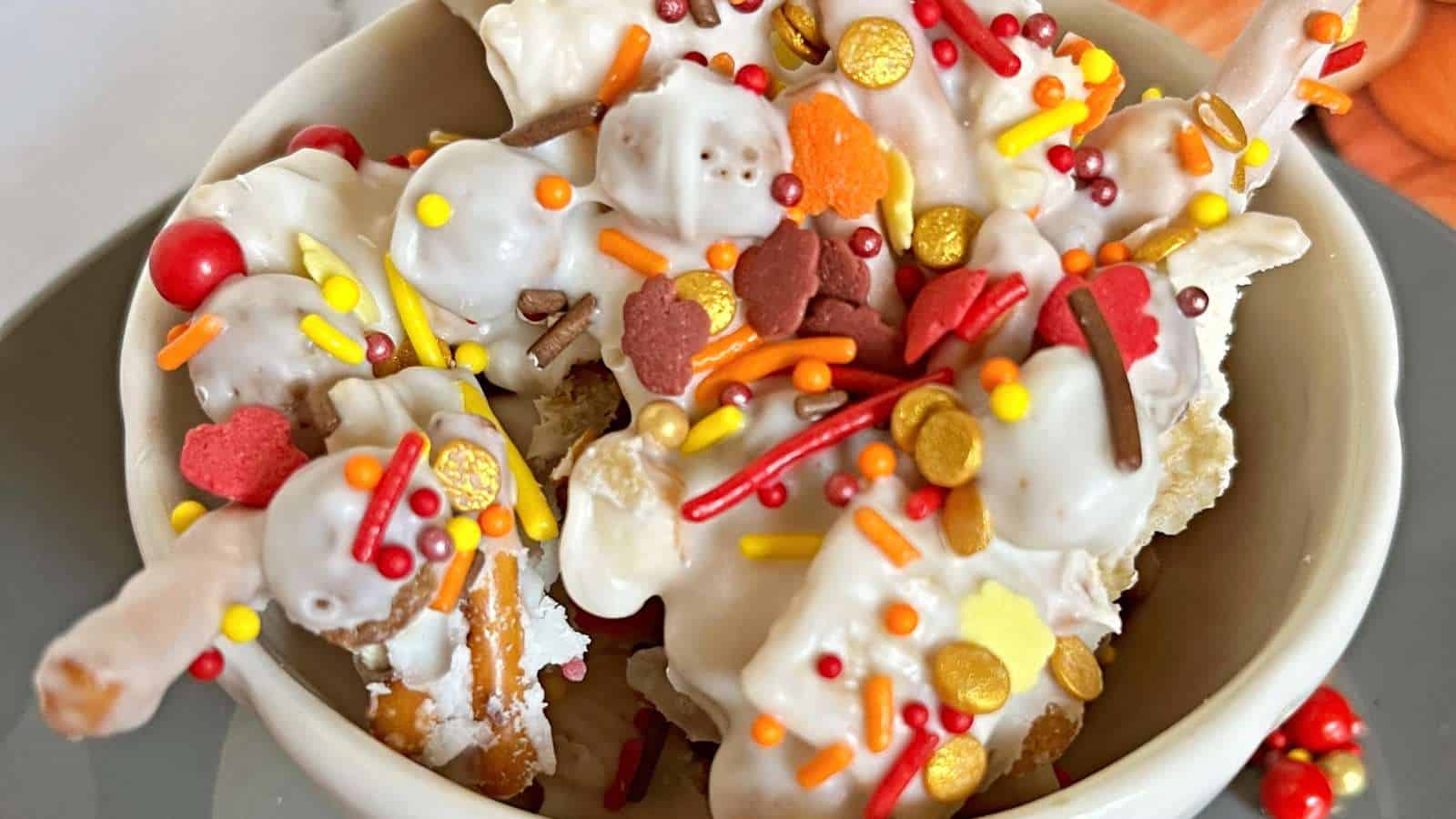 A bowl of pretzel pieces coated in white chocolate and topped with colorful fall-themed sprinkles.