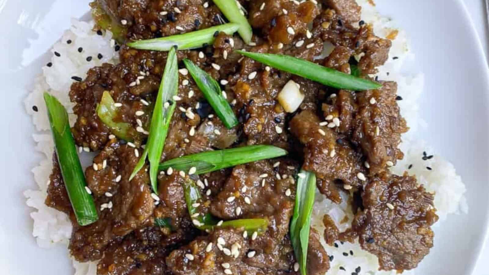 Beef stir-fry with green onions and sesame seeds served over white rice on a white plate.