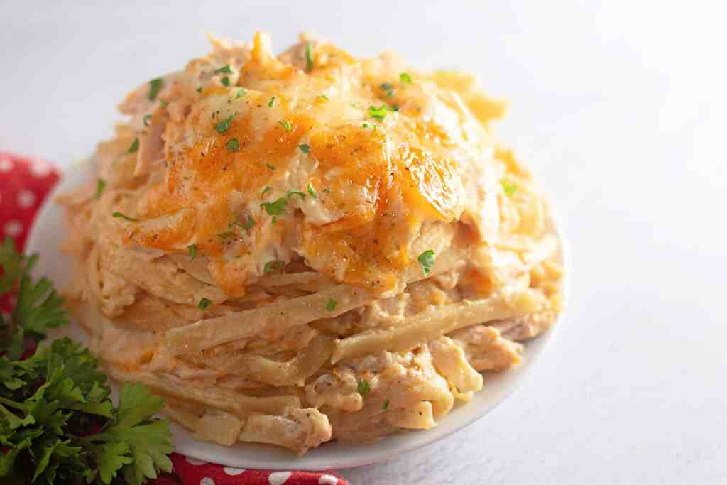 A plate of cheesy chicken and potato casserole topped with melted cheese and garnished with chopped parsley.