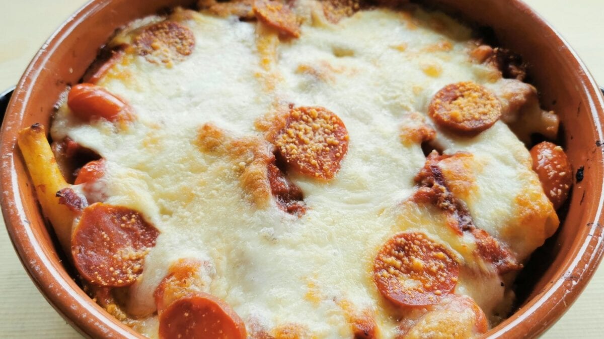 A baked dish in a round brown ceramic bowl, topped with melted cheese and slices of pepperoni.