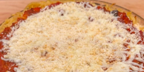 A close-up of a baked dish topped with marinara sauce, melted mozzarella cheese, and grated Parmesan cheese in a glass pie dish.