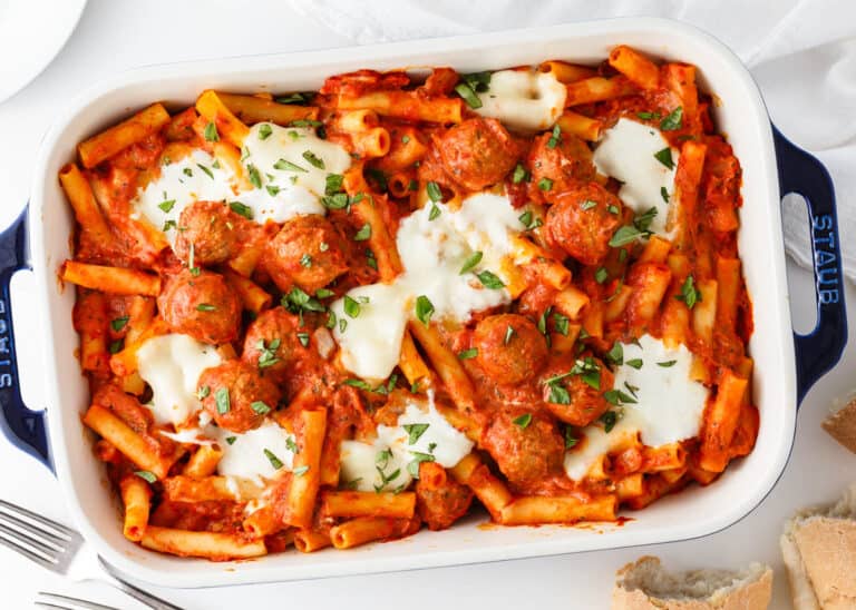 Baked ziti with meatballs, melted cheese, and tomato sauce garnished with chopped herbs in a rectangular dish.