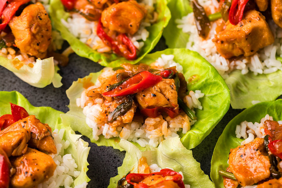 Chicken, rice, and sliced red peppers served on lettuce leaves, creating lettuce wraps on a dark surface.