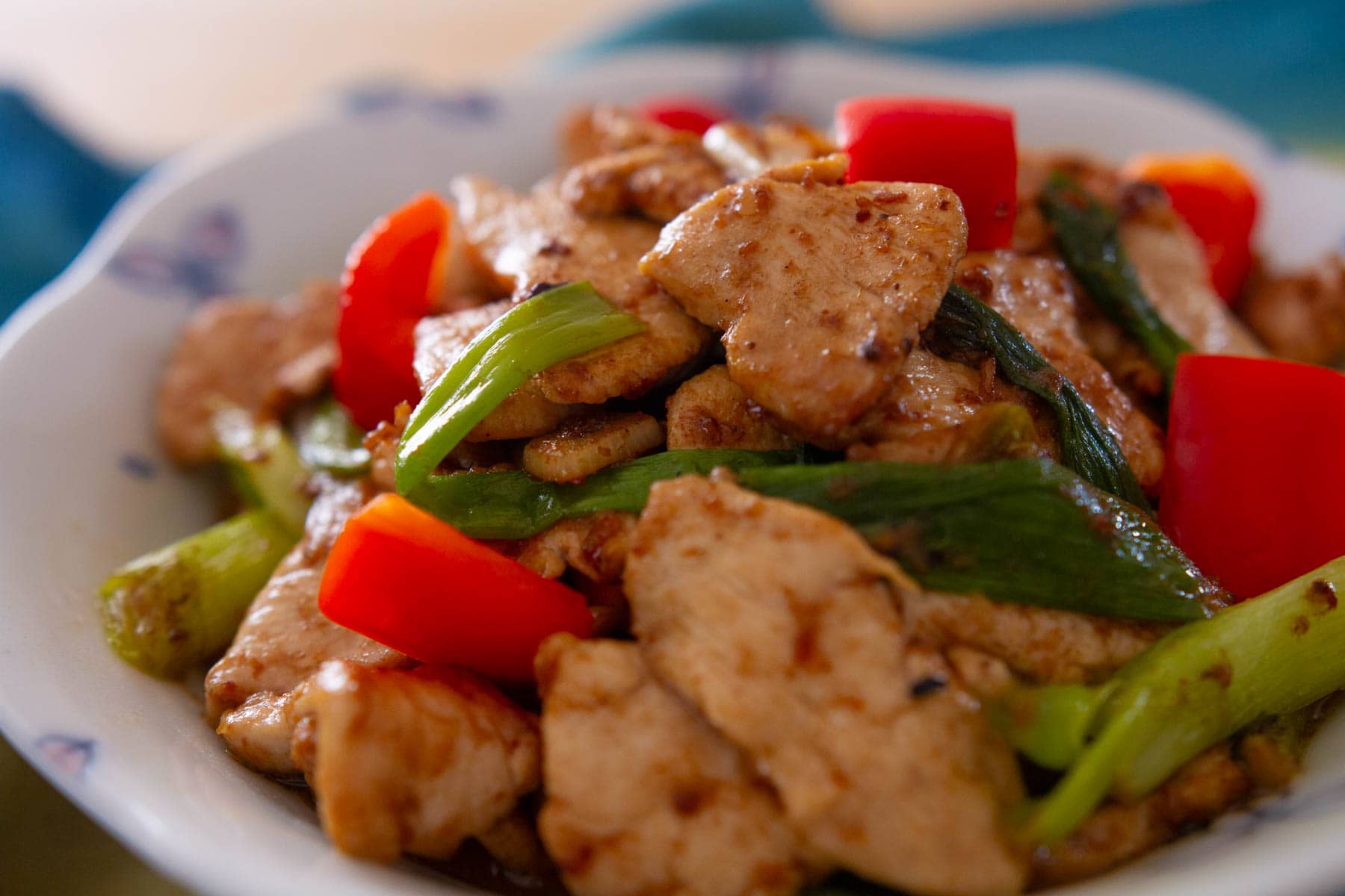 A plate of stir-fried chicken with red bell peppers and green onions, served on a white dish.