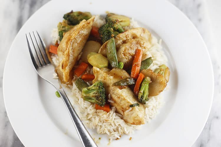 A plate of white rice topped with steamed vegetables and pieces of chicken, served with a fork on the side.