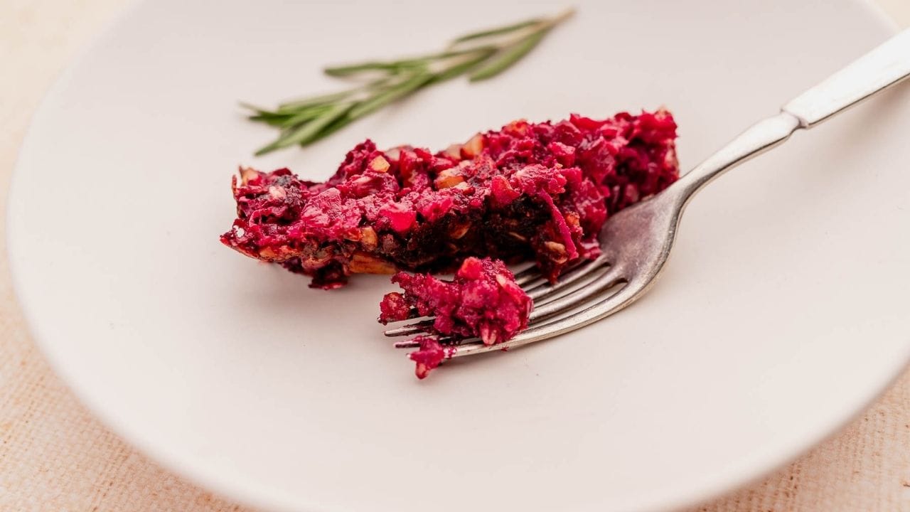 A fork holding a portion of berry crumble dessert on a white plate, with a sprig of rosemary in the background.
