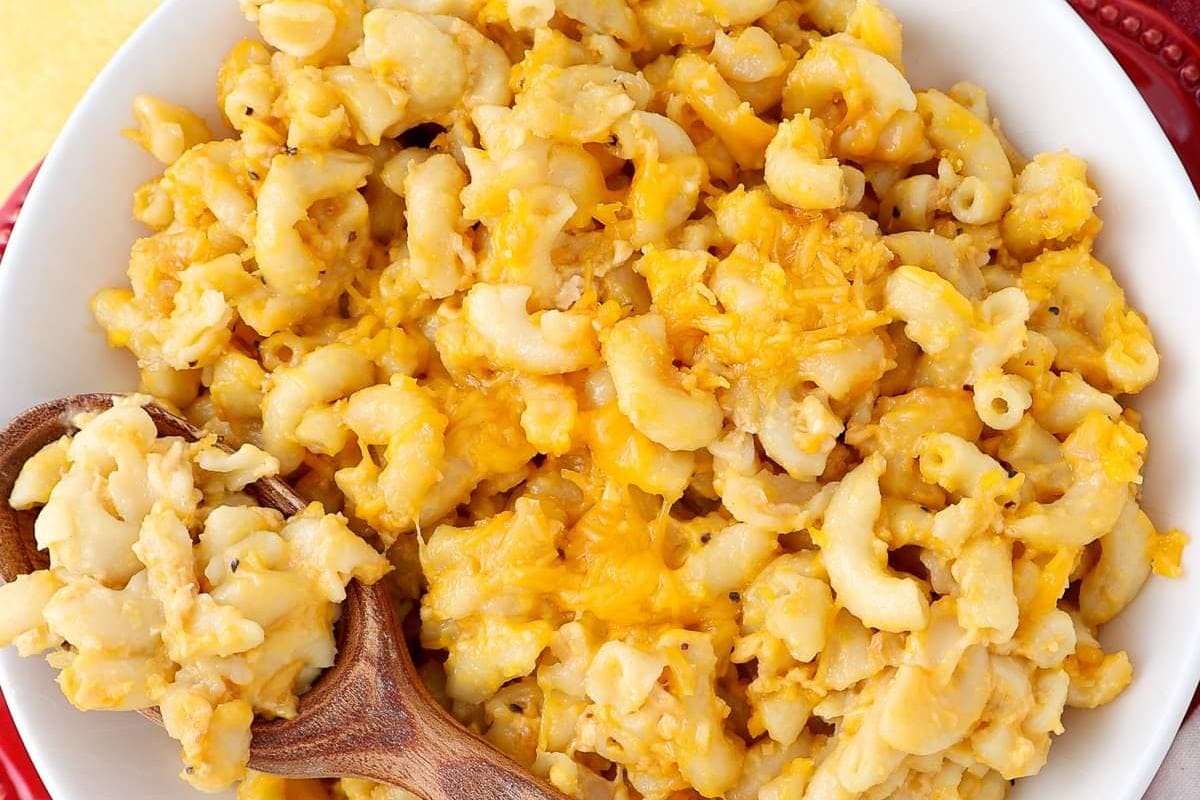 A close-up of a bowl filled with macaroni and cheese, with a wooden spoon scooping some of the cheesy pasta.