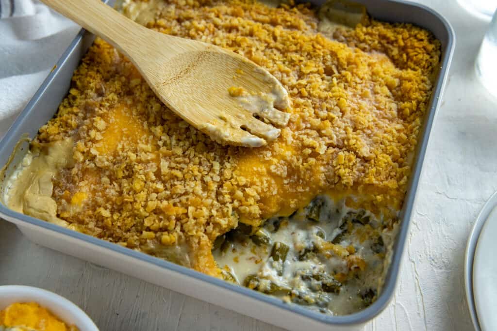 A casserole dish filled with cheesy, crumb-topped baked casserole, partially served with a wooden spoon resting on top.