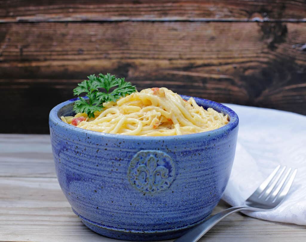 A blue ceramic bowl filled with spaghetti topped with grated cheese and parsley sits on a wooden surface next to a fork.