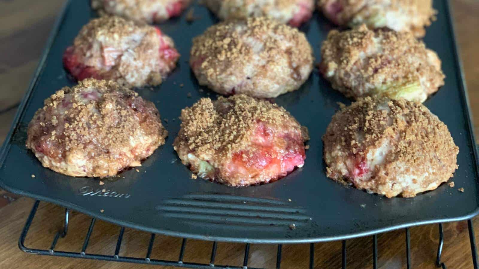 A muffin tin filled with baked fruit muffins topped with a crumbly brown streusel, cooling on a wire rack.