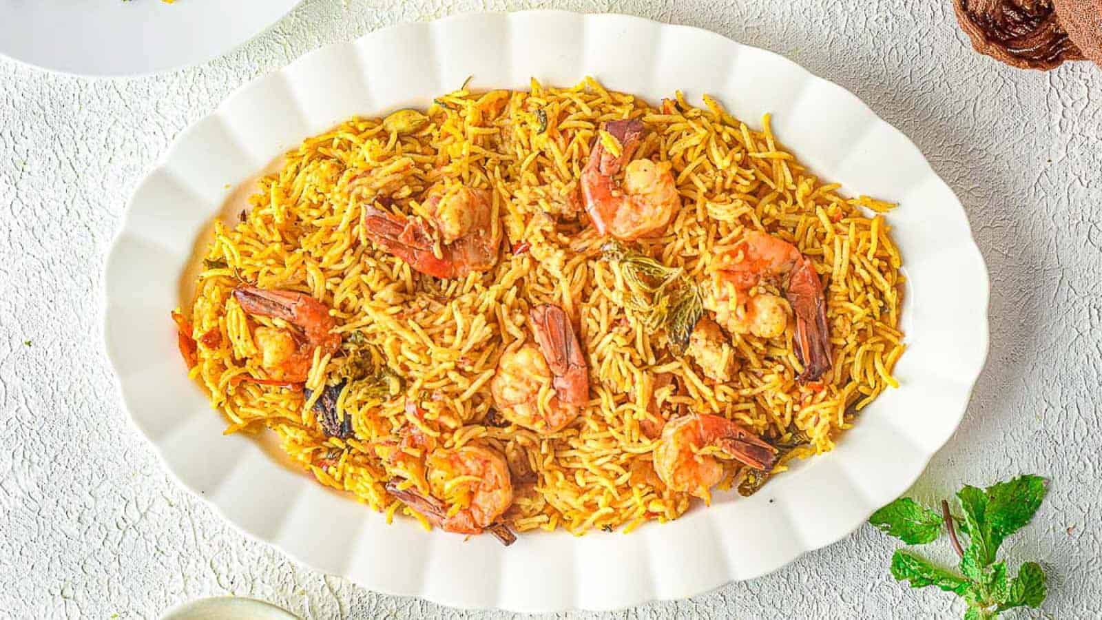 Oval white plate filled with shrimp biryani, featuring rice, shrimp, and visible spices, placed on a light textured surface.