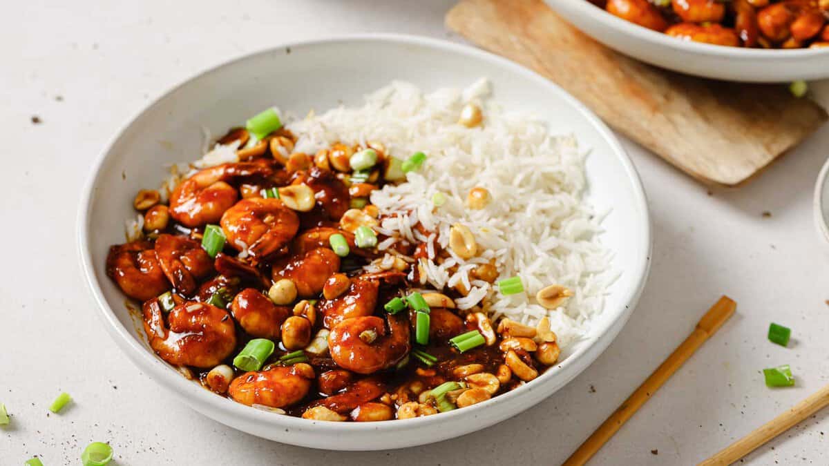 A bowl of white rice served with shrimp in a dark sauce, garnished with chopped green onions and peanuts.