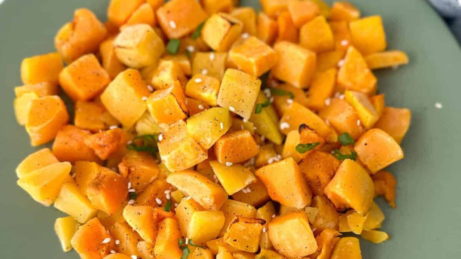 A plate of roasted diced yellow and orange root vegetables, garnished with a few green herbs and sprinkled with sesame seeds.