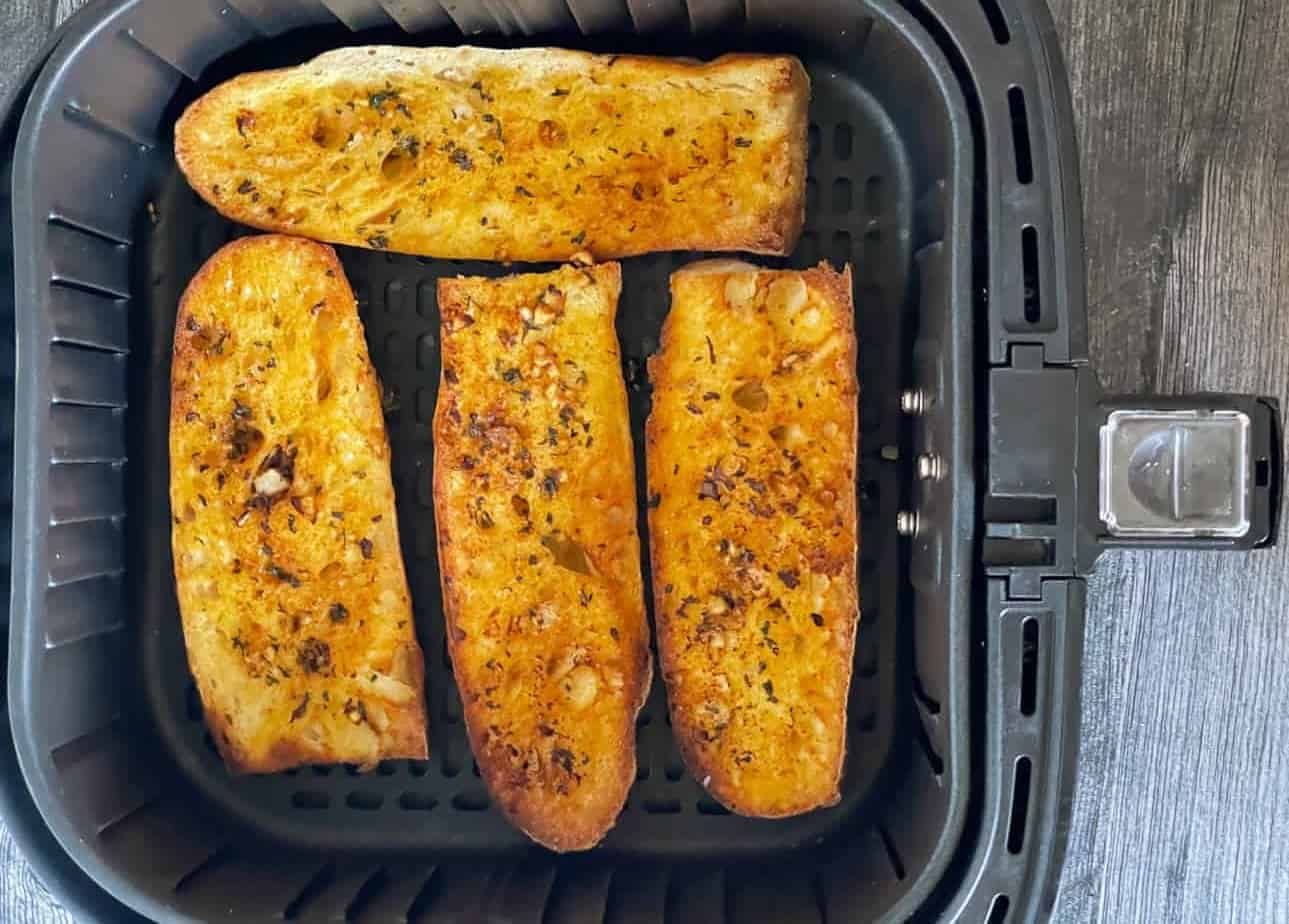 Four pieces of seasoned garlic bread are arranged in a single layer inside an air fryer basket.