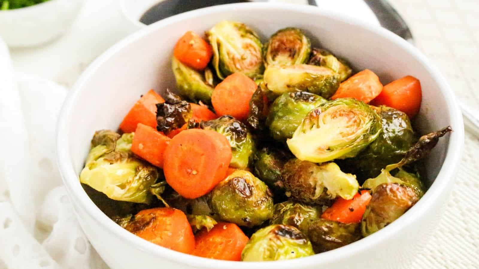 A white bowl filled with roasted Brussels sprouts and sliced carrots.