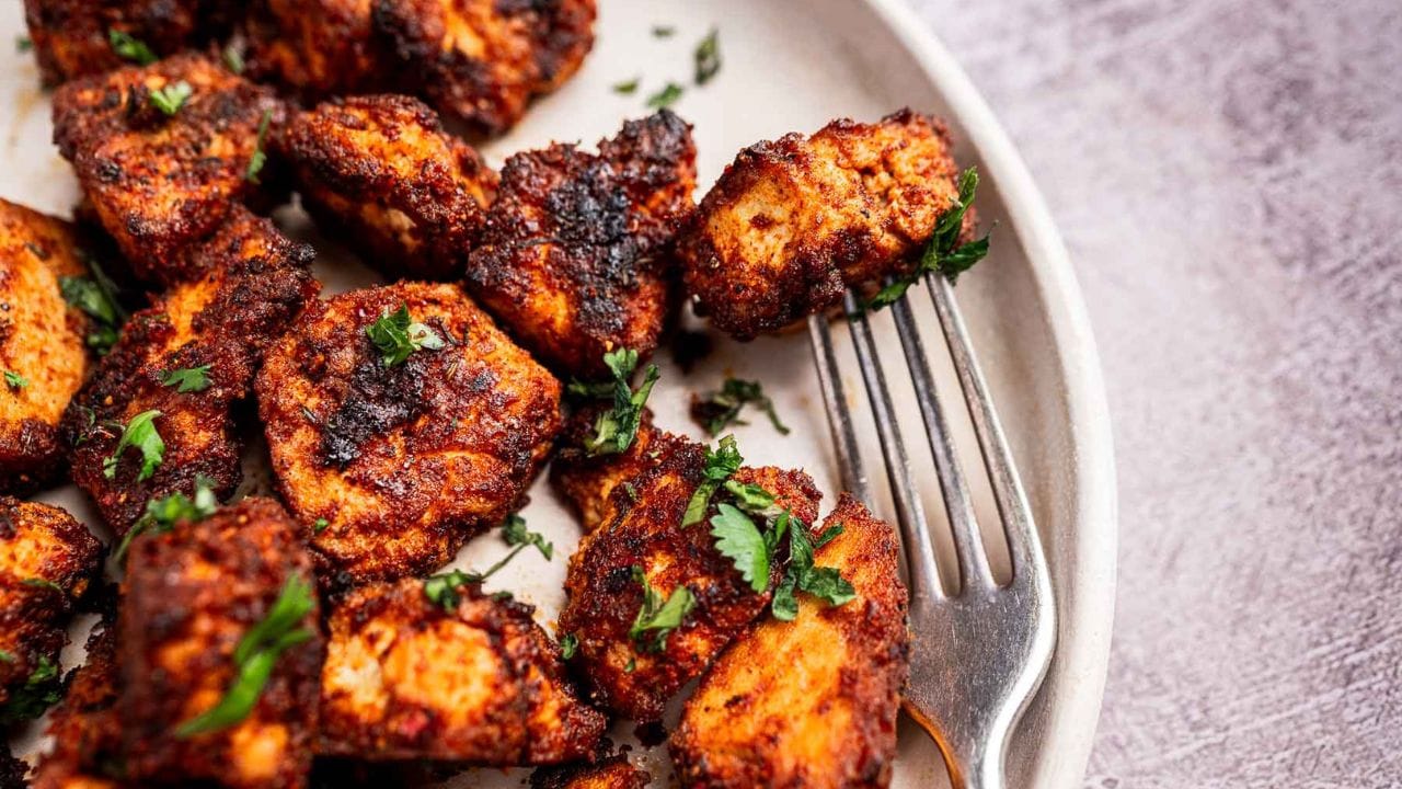 A plate of seasoned, browned chicken pieces garnished with chopped herbs, with a fork placed among the pieces.