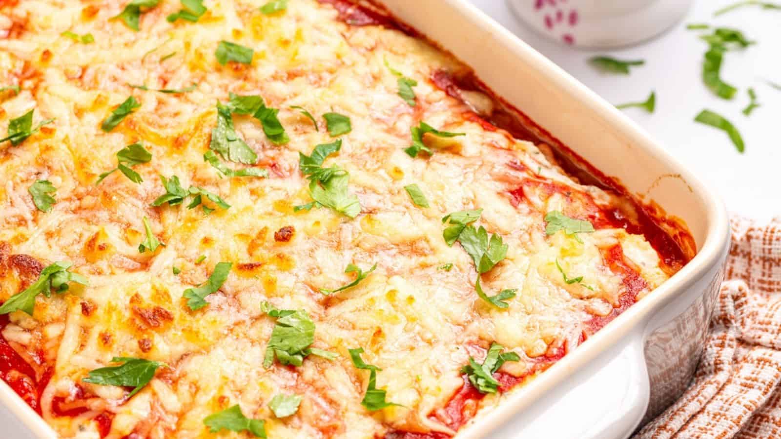A baked casserole dish filled with cheesy, golden-brown lasagna topped with fresh green herbs.