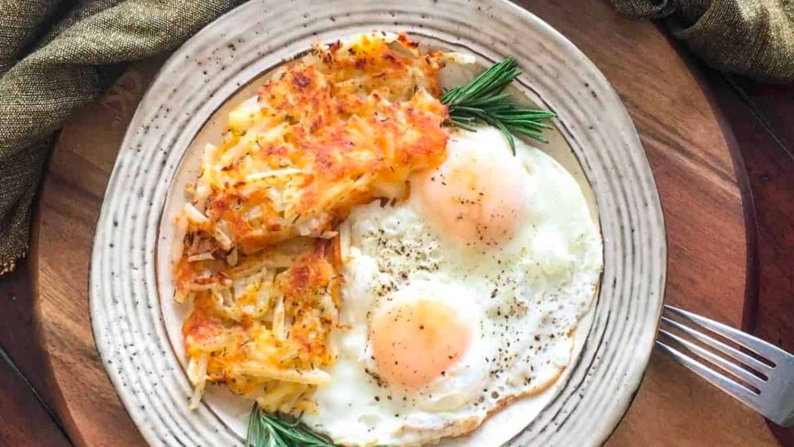 A plate with two sunny-side-up eggs, a portion of crispy hash browns, and sprigs of rosemary, served on a patterned ceramic dish.