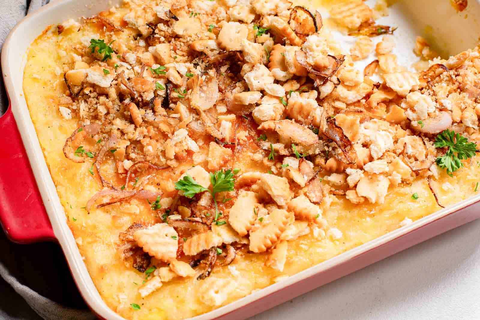 A baked casserole topped with crushed crackers, herbs, and caramelized onions, in a red-edged rectangular dish.