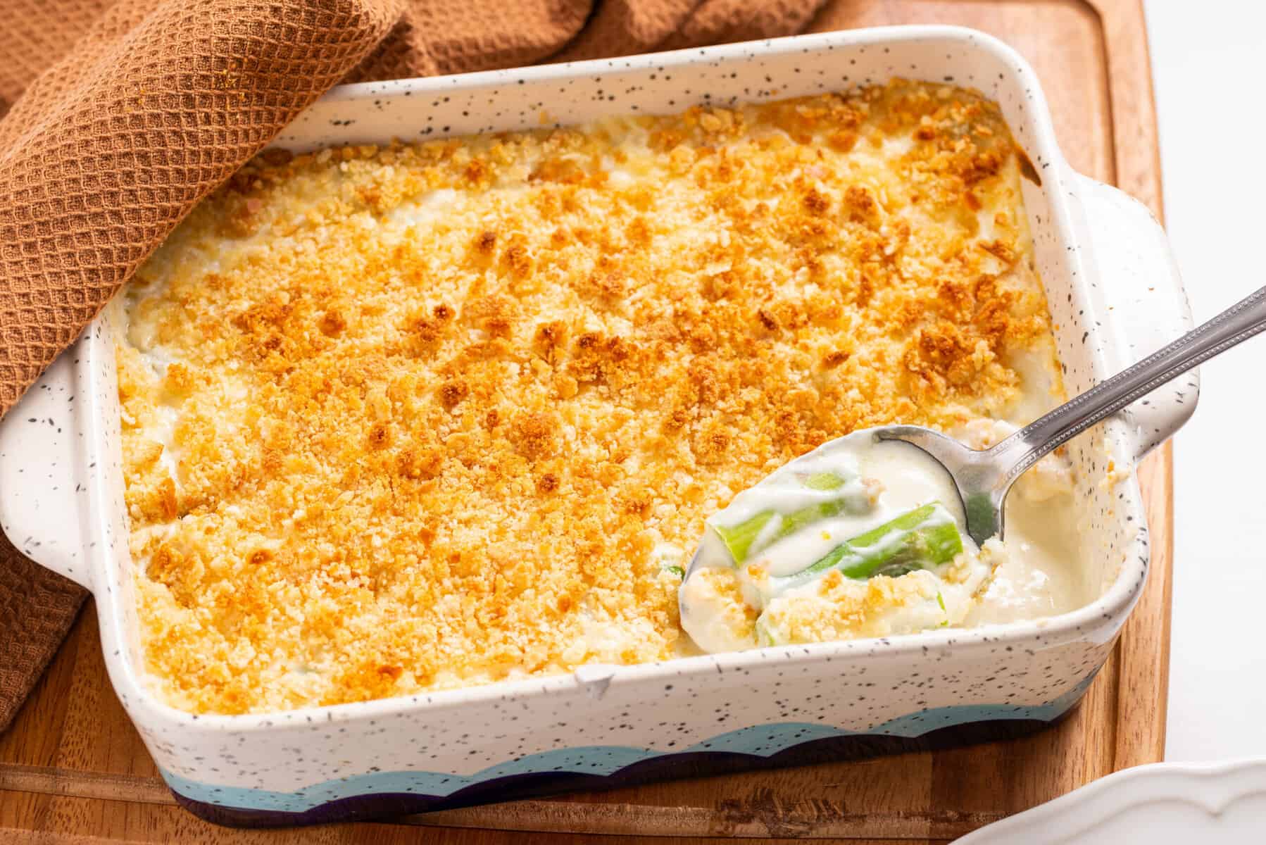 A casserole dish filled with creamy baked casserole topped with golden breadcrumbs, with a serving spoon scooping out a portion.