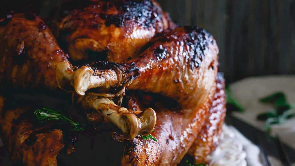 Close-up of a roasted turkey with browned, crispy skin, garnished with fresh herbs and placed on a platter.