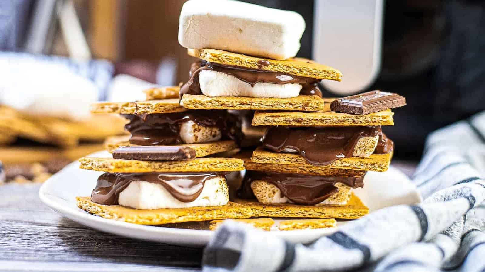 A plate stacked with smores made of graham crackers, melted chocolate, and toasted marshmallows on a wooden table.