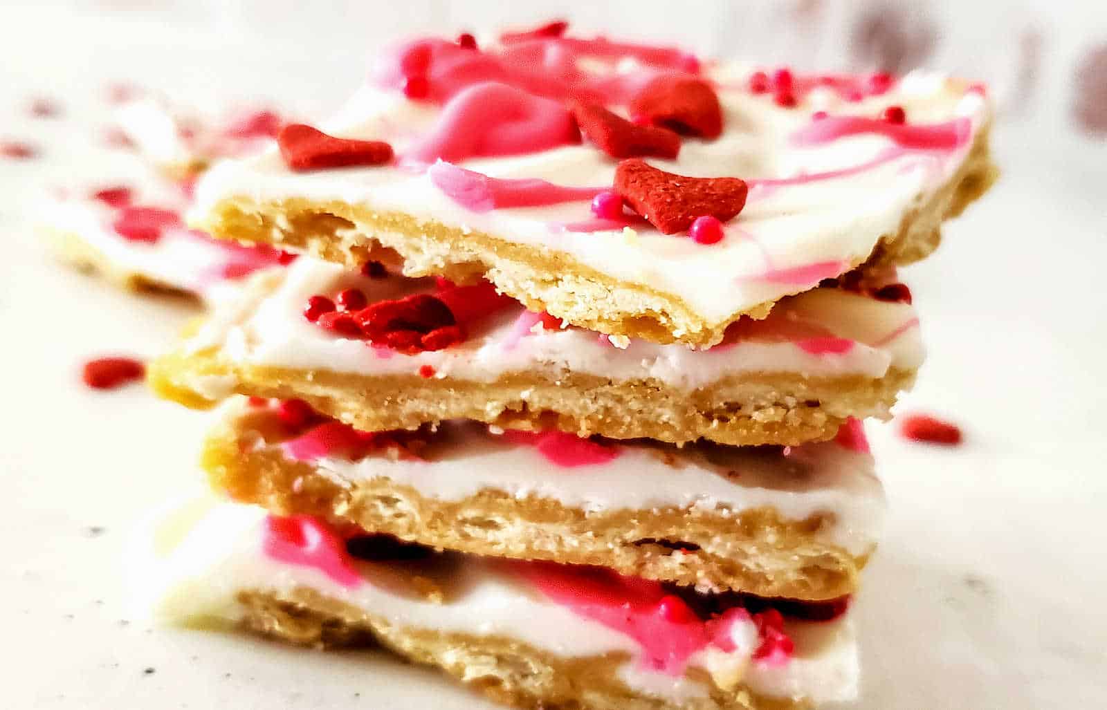A stack of white chocolate bark pieces with red and pink sprinkles and heart-shaped decorations on a white surface.