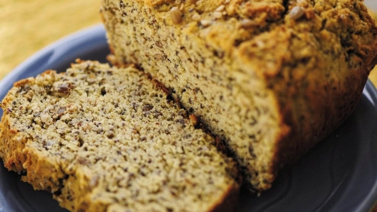 A loaf of nut bread sits on a plate with one slice cut and partially separated from the rest of the loaf.