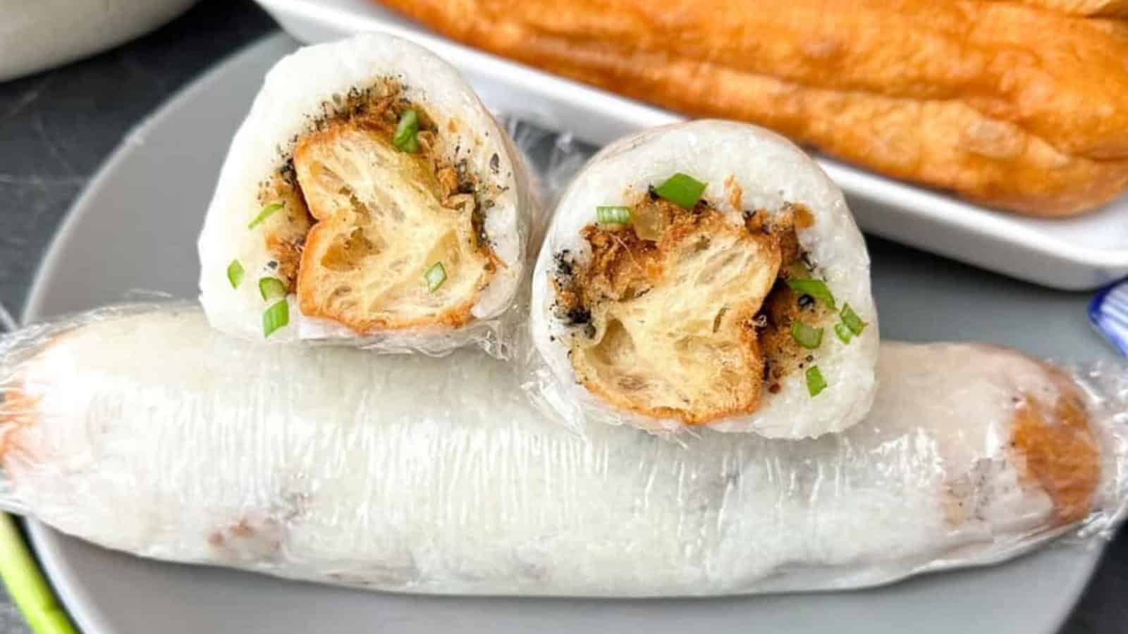 A plate with a wrapped Vietnamese sticky rice roll filled with fried dough, cut in half to show the filling, garnished with green onions.