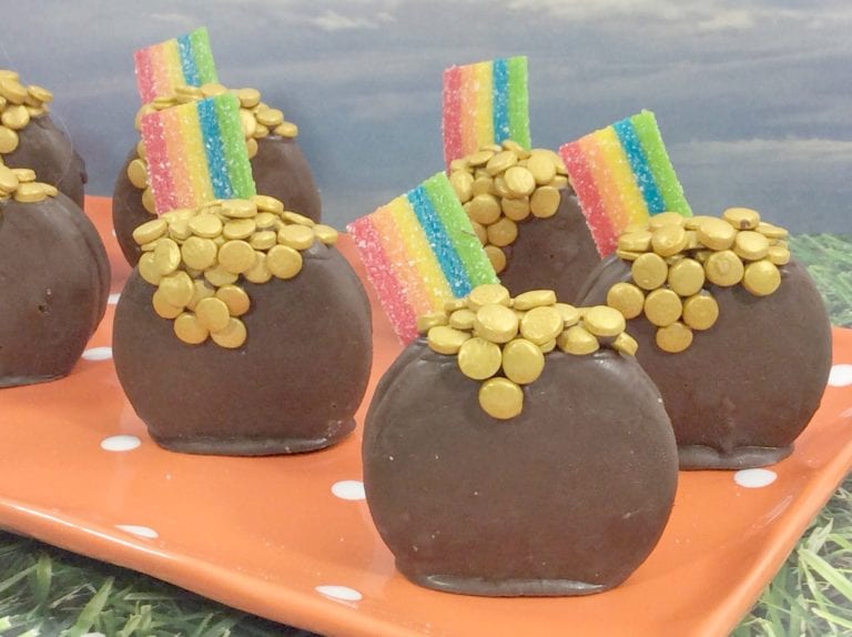Chocolate treats shaped like pots, topped with gold candy coins and strips of rainbow candy, arranged on an orange polka-dot plate.
