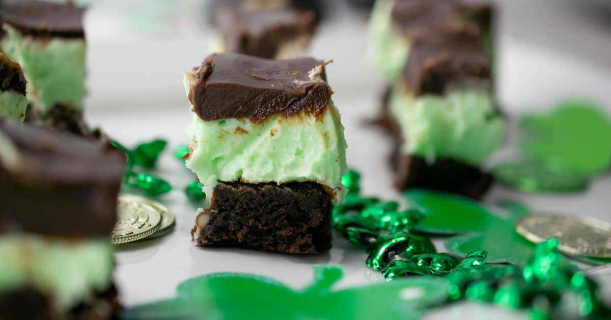 Close-up of a mint chocolate brownie with a chocolate topping, surrounded by green shamrock decorations and gold coins.