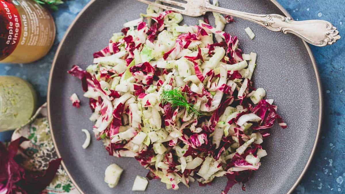 A plate of chopped radicchio and fennel salad garnished with dill, served on a gray dish with a fork.