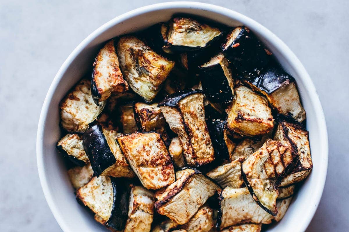 A white bowl filled with roasted eggplant cubes, showing a golden-brown and slightly charred exterior.