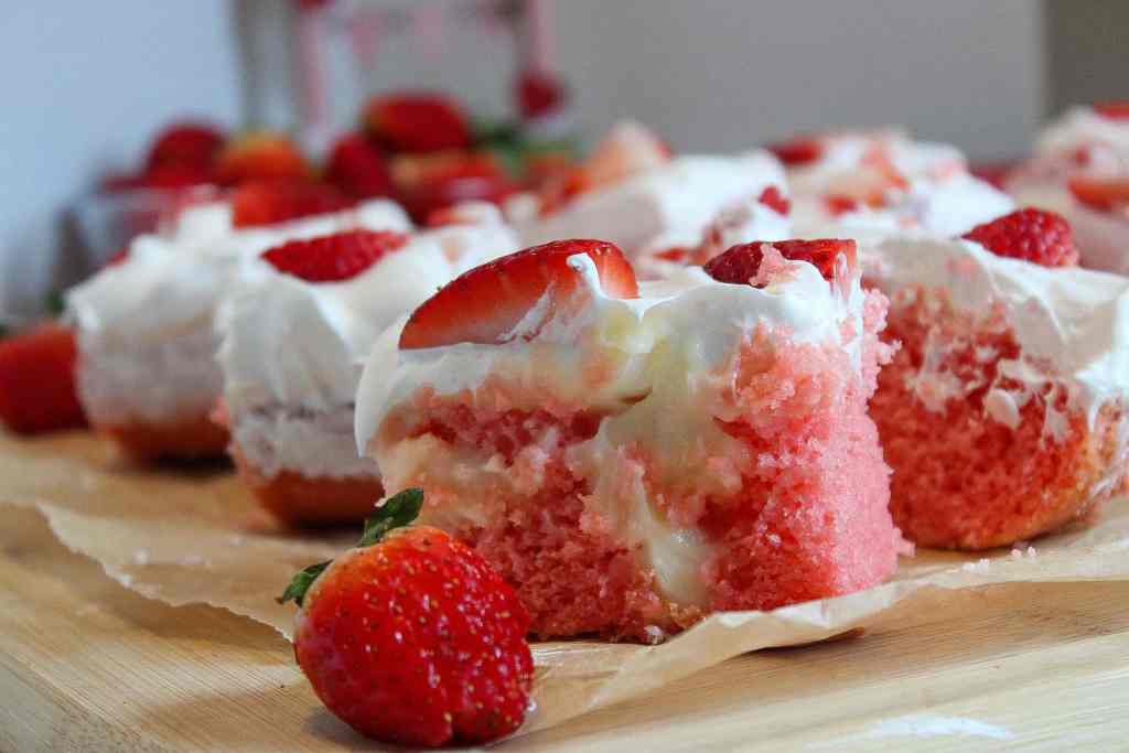 Slices of strawberry cake with whipped cream and fresh strawberry pieces on top, arranged on parchment paper.