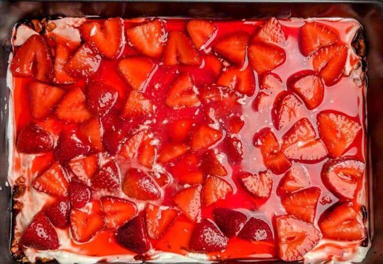 Rectangular dessert topped with sliced strawberries and a glossy red glaze, set in a dark baking dish.