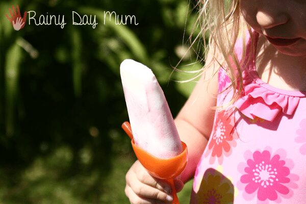 A young child in a pink floral swimsuit holds a homemade popsicle outdoors.