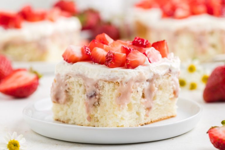 A slice of sponge cake topped with whipped cream and chopped fresh strawberries on a white plate.