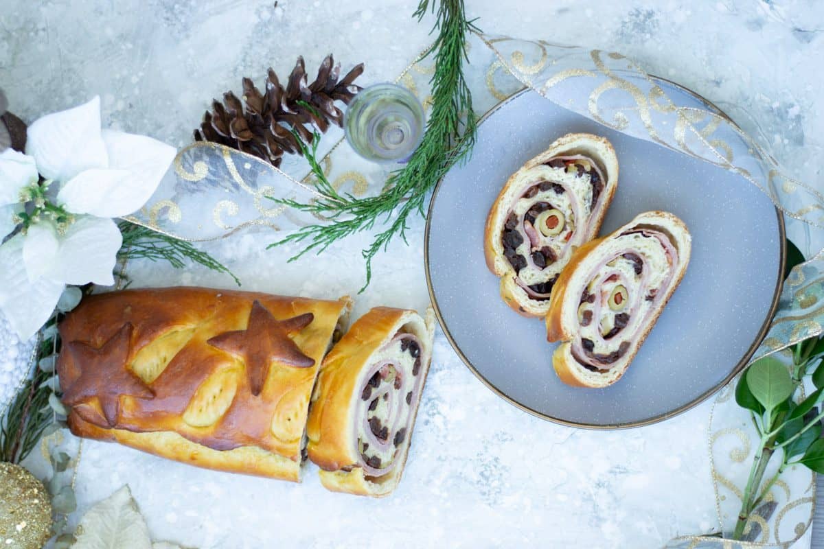Sliced holiday bread with swirled filling, garnished with star shapes, served on a gray plate, surrounded by festive decorations and greenery.